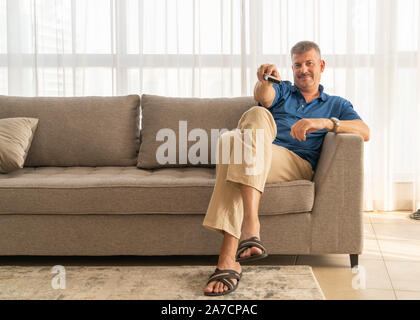 middle aged man sitting on a sofa and watching TV Stock Photo