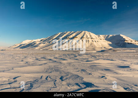 Arctic winter landscape at Kapp Ekholm, snow formed by the wind to a nice texture. Snow covered mountains and blue sky in the background. A sunny day Stock Photo