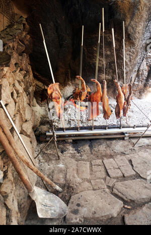 An open fire with a  roast suckling pig cooked on a spit in a typical rustic family run  agriturismo in Sardinia Italy Europe Stock Photo