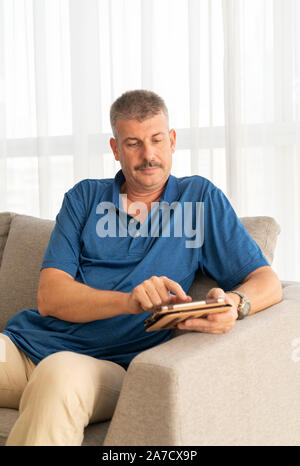 middle aged man working on his tablet on a sofa Stock Photo