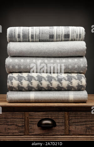 Portrait view of 5 grey luxury folded throws shot on a wooden sideboard, above a draw, with a grey background Stock Photo