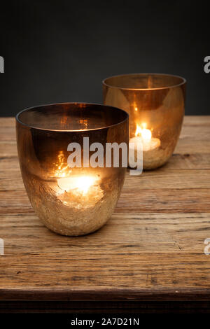 2 smoked glass tea light holders and glowing candles, shot on a wooden table, with a dark grey background Stock Photo