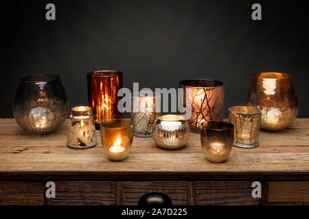 A group of glass tea light holders and glowing candles, shot on a wooden table, with a dark grey background Stock Photo
