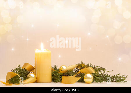 Christmas copy space with a lit yellow candle, pine branches, golden satin ribbon and gold-colored Christmas balls on a light patterned background Stock Photo