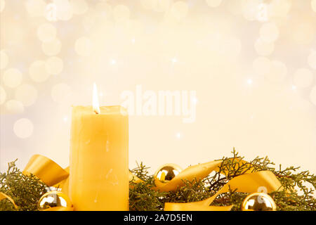 Christmas copy space with a lit yellow candle, pine branches, golden satin ribbon and gold-colored Christmas balls on a light patterned background Stock Photo