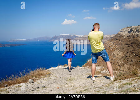 Young  man photographs a beautiful woman on the background of the sea and the island of Santorini Stock Photo