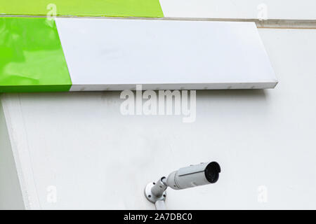 White surveillance camera on white wall with blank tablet above it Stock Photo