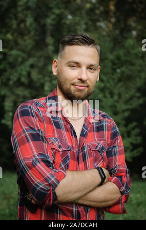 Outdoor portrait of relaxed handsome young man with beard in the park on green trees background. Hipster style concept. Stock Photo