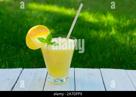 Bright melon smoothie with mint and lemon on a background of fresh green grass. Copy space. Concept of summer cooling drinks. Stock Photo