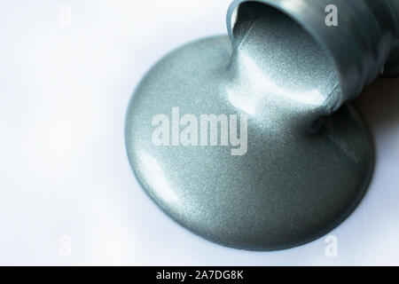 Silver paint poured from a bottle on a white background. Copy space. Stock Photo