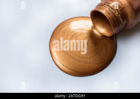Copper-colored paint pouring from a bottle on a white background. Copy space. Stock Photo