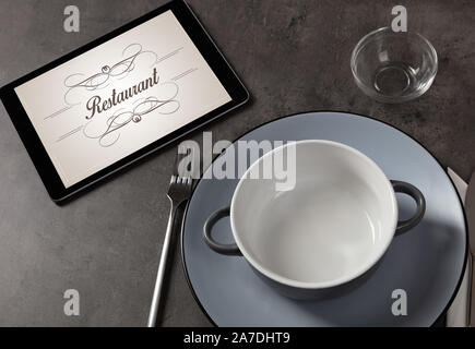 Tablet with stylish restaurant logo and laid table Stock Photo