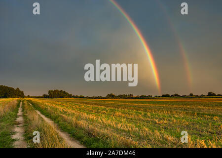 Two rainbows in the cloudy sky, horizon and dirt road in the field, Nowiny, Poland Stock Photo