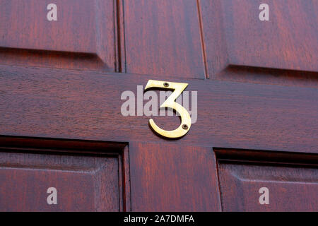 Large and elegant bronze house number 3 on a reddish wooden front door Stock Photo