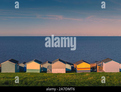 Colourful beach huts along a grass verge in Tankerton, Whitstable, Kent, UK. The sea and sky are blue on a sunny winter day, late in the afternoon. Th Stock Photo