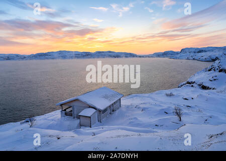 A wooden house, Barents sea at sunrise in Teriberka, Murmansk Region, Kola Peninsula. Russia.  Strong fog or smoke over sea. Stock Photo