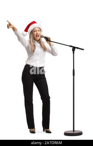 Full length portrait of a female singer with a microphone and a santa claus hat isolated on white background Stock Photo