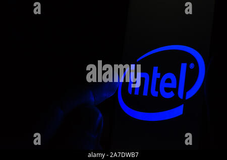 Intel logo on a smartphone screen in a dark room and a finger touching it. Stock Photo