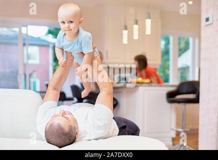 Concept of family, father and baby playing on the sofa, happy childhood. Indoor shot in the kitchen. child in his arms, the child throws up to the cei Stock Photo