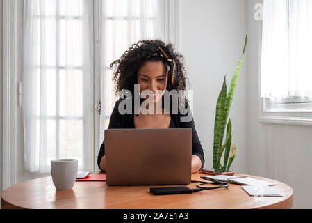 Shot of young latin woman working at home with laptop and documents Stock Photo