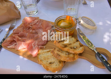 Fresh Parma ham on a wooden board, served with bread and pickled vegetables. Stock Photo