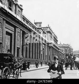 A vintage late Victorian or early Edwardian black and white photograph showing buildings and people on the streets of London, England. A horse drawn carriage is also in the photo. Stock Photo