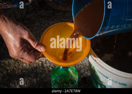 Old woman's hands pouring juice from pan in bottle via funnel Stock Photo