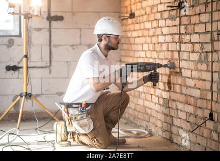 Handyman uses jackhammer, for installation, professional worker on the construction site. The concept of electrician and handyman. House and house rec Stock Photo