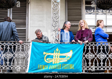 New Orleans, USA - April 23, 2018: Old town street in Louisiana city with closeup of people on balcony by French Quarter Festival banner sign Stock Photo