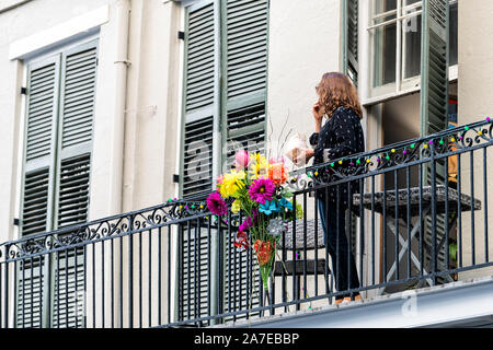 New Orleans, USA - April 23, 2018: Old town Royal street in Louisiana famous city balcony with woman and flower decorations by shutters on house build Stock Photo