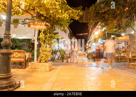 SKIATHOS GREECE - JULY 30 2019; People blurred as they walk at night under light in streets alive with tourists visiting restaurants and shops on Gree Stock Photo