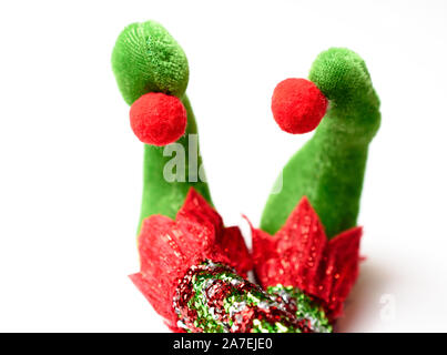 Adorable plush elf feet wearing red white and green pointy shoes with pom poms and glittered stockings with legs crossed Stock Photo