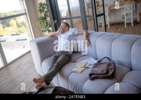 Businessman sitting on sofa and yawning while feeling sleepy Stock Photo
