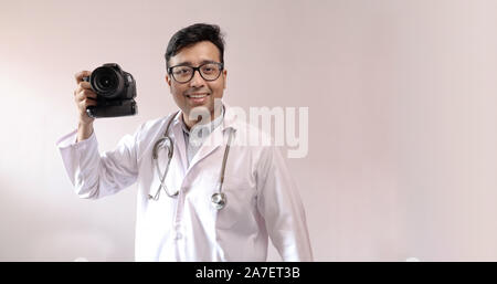 male indian doctor in white coat and stethoscope and a DSLR camera in hand, doctor as a photographer Stock Photo