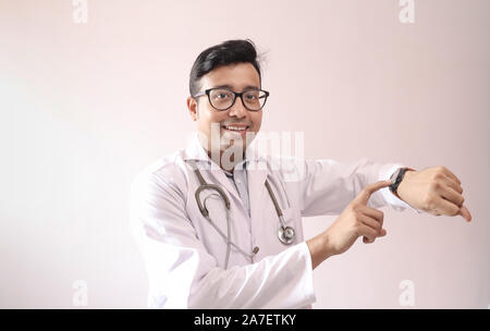 male indian doctor in white coat and stethoscope touch screen and checking notification in smart watch Stock Photo