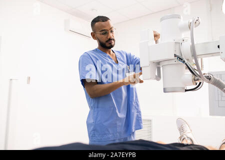 Bearded young mixed-race man in blue uniform using new medical equipment Stock Photo
