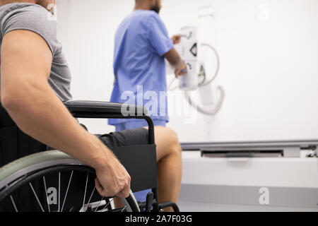 Arm of sick sportsman with broken leg sitting on wheelchair in front of doctor Stock Photo