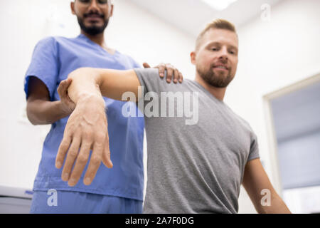 Masseur in blue uniform holding sick arm of patient while massaging it Stock Photo