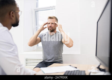 Young bearded man touching his head while complaining on permanent headache Stock Photo