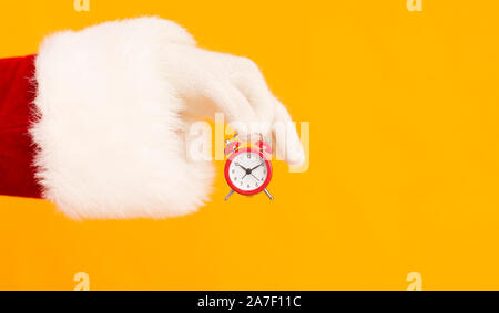 Santa hand holding small red alarm clock with time on orange Stock Photo