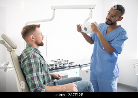 Young doctor in uniform holding medical equipment or lamp in front of patient Stock Photo