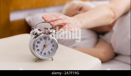 Senior woman turning of alarm clock, lying in bed, panorama Stock Photo