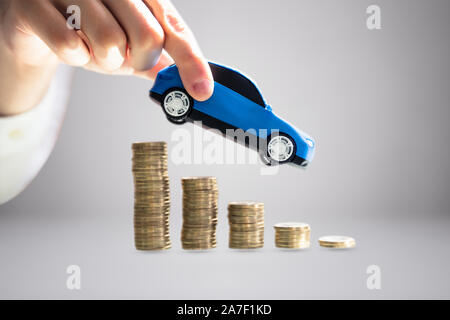 Close-up Of A Person's Hand Holding Blue Model Toy Car Over Stacked Of Golden Coins Stock Photo