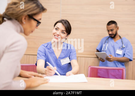 Clinician in uniform smiling at patient while pointing at medical document Stock Photo
