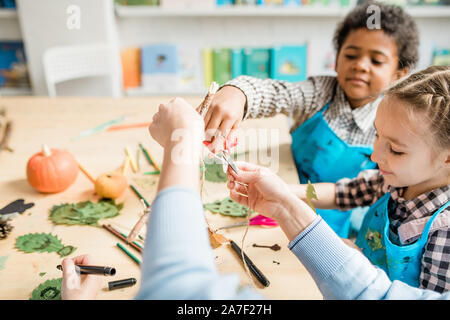 Cute schoolboy cutting thread with scissors while helping his teacher at lesson Stock Photo