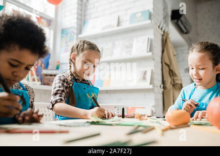 Two cute diligent girls and African boy drawing with highlighters by desk Stock Photo