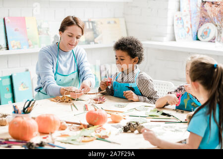 Young teacher pointing at stick with several halloween decorations at lesson Stock Photo