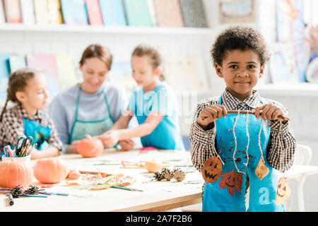 African schoolboy in blue apron holding stick with halloween decorations Stock Photo
