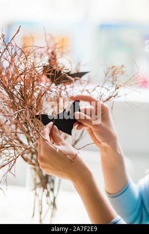 Hands of woman with black handmade bat by dry branches decorating her home Stock Photo