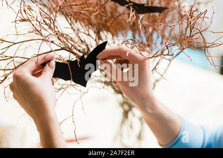 Hands of girl holding black paper bat by dry branches while decorating them Stock Photo